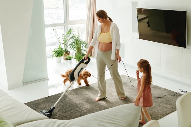 Pregnant woman vacuuming with a child and dog in a living room